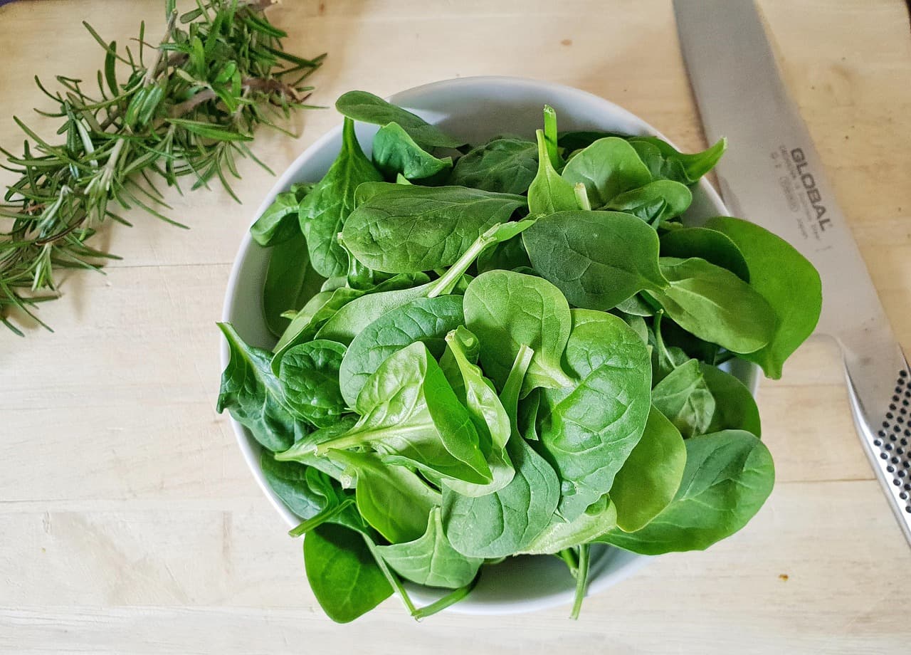 Fresh spinach leaves and sprigs of rosemary on a kitchen counter during meal preparation