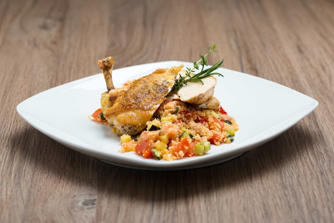 A plate of roast meat with vegetable couscous and fresh herbs, on a white plate