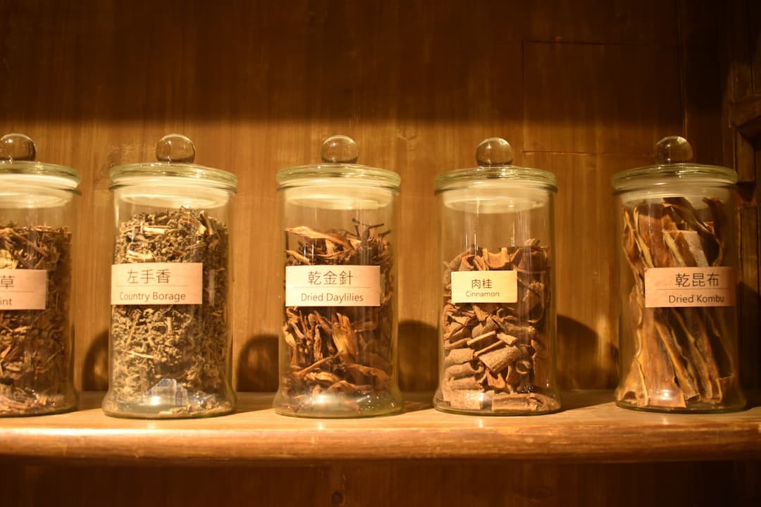 Glass jars of dried herbs lined up on a wooden shelf in soft daylight