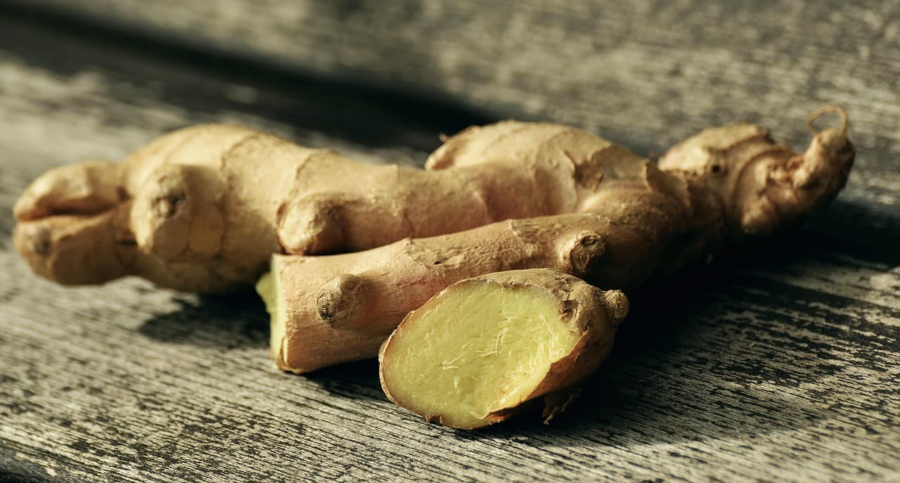 Fresh ginger root with a cut cross-section on a dark wooden surface