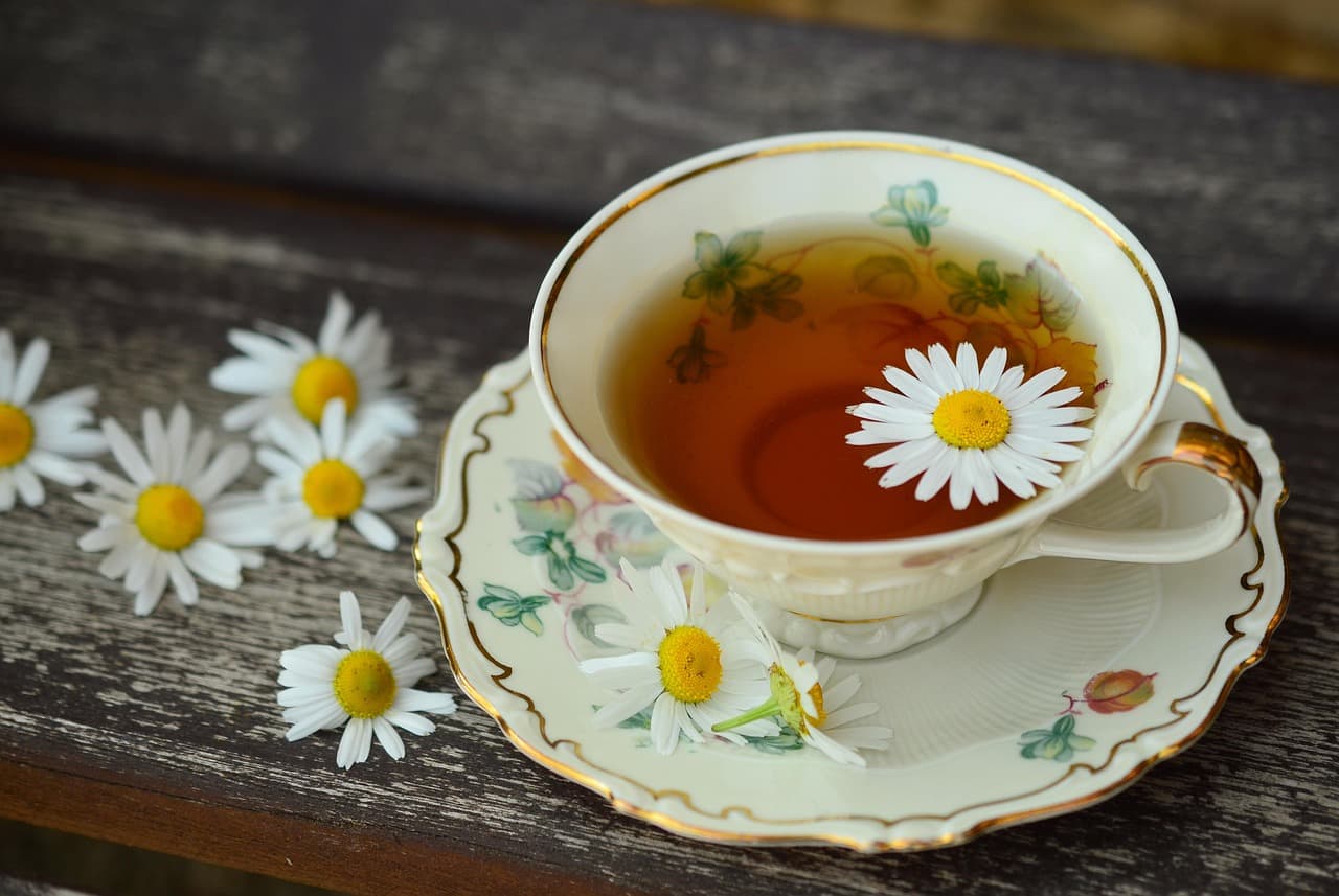 Porcelain teacup of warm chamomile herbal tea on a wooden surface, soft natural light, still-life composition