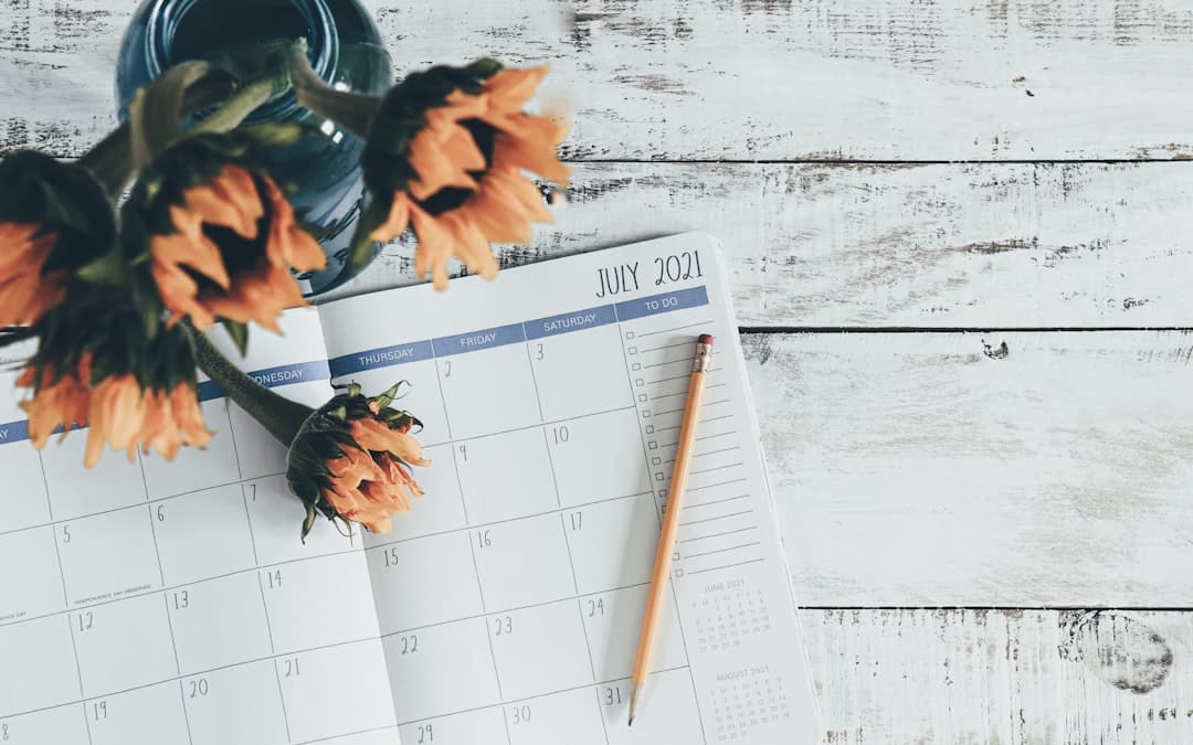 An open monthly planner on a wooden surface in soft daylight, with a bouquet of sunflowers resting above it
