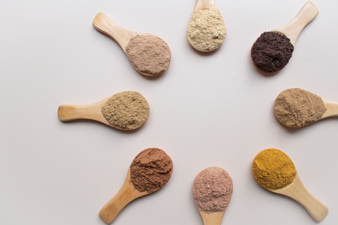 Several wooden spoons laid side by side, each holding a different coloured powder