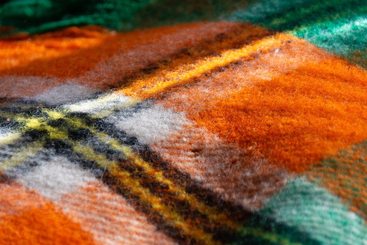 A close-up of a soft striped wool blanket in warm orange, brown and green