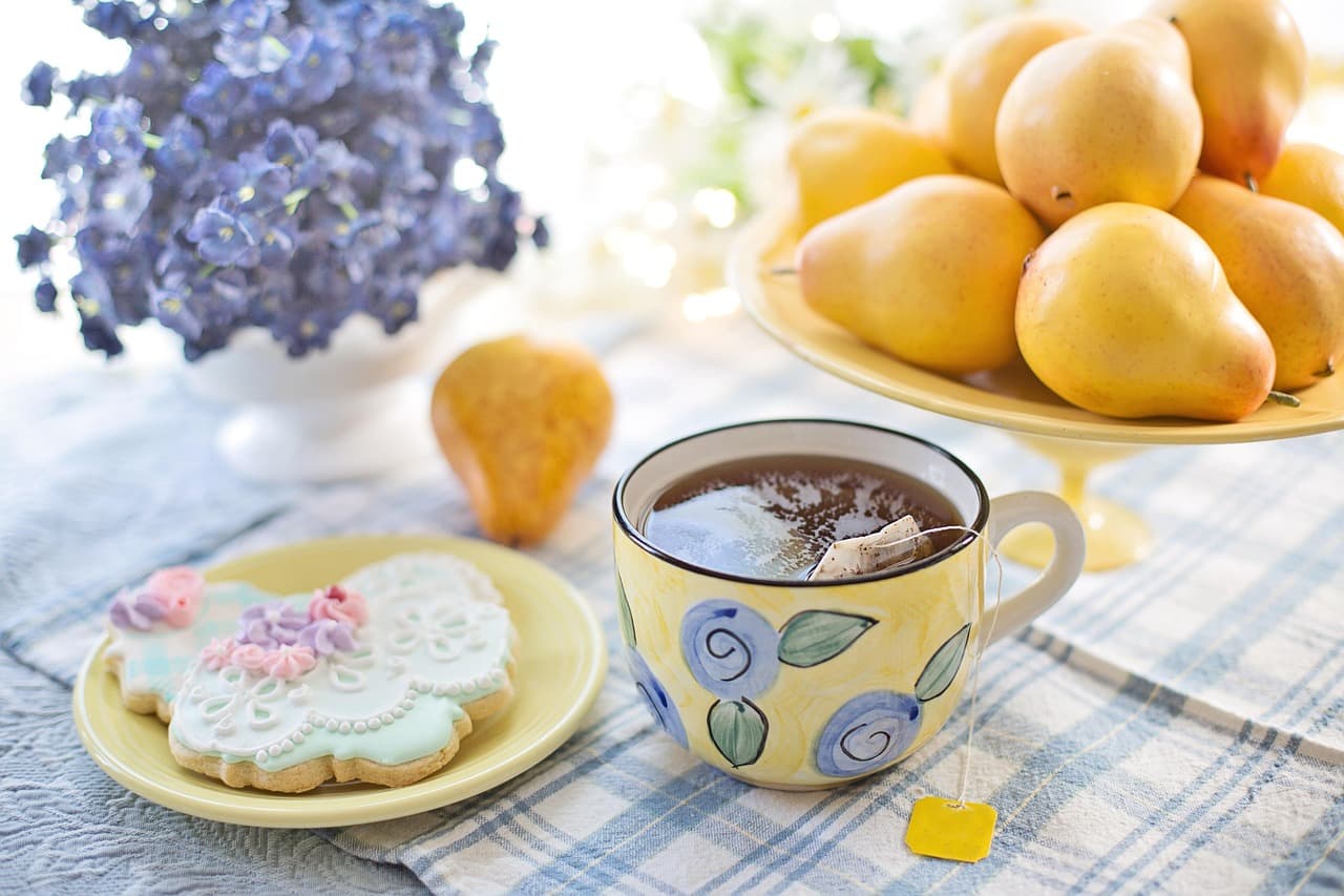 A warm still life of tea in a cup beside biscuits and ripe pears in soft daylight