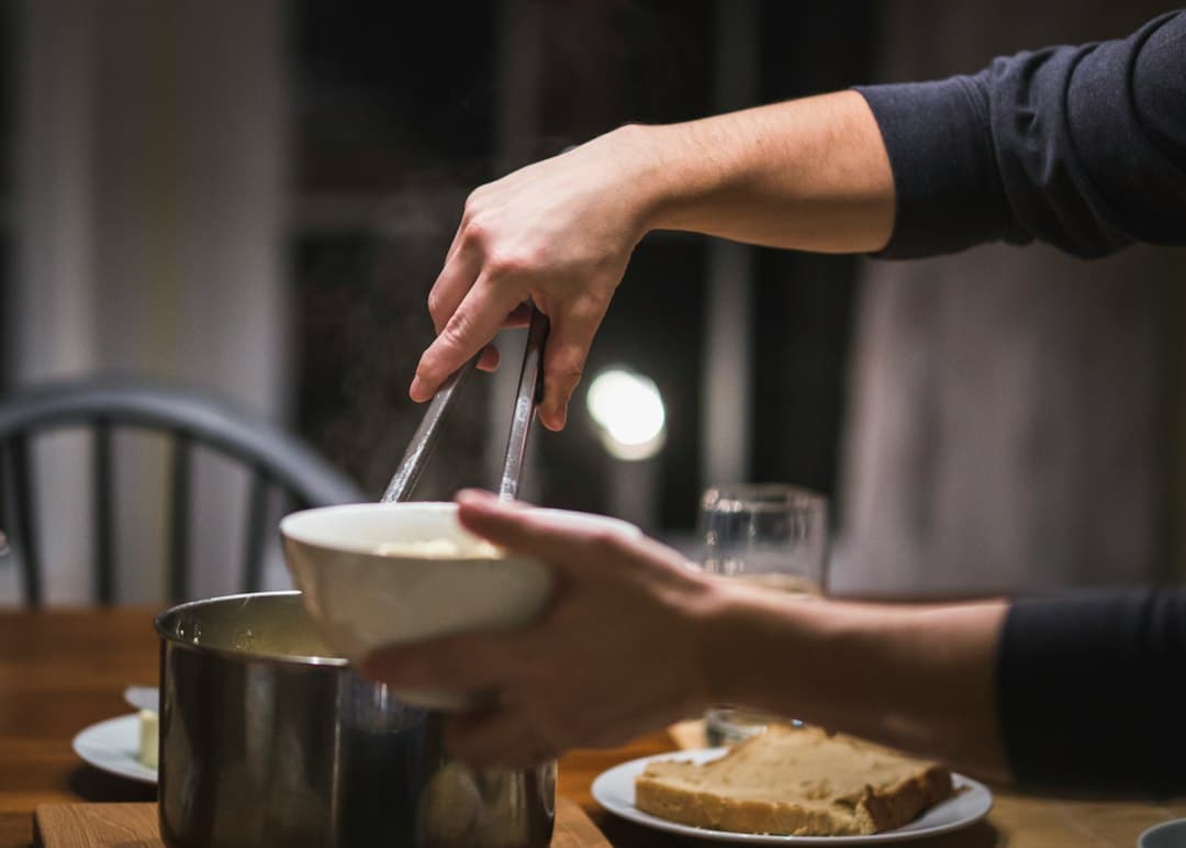 Hands setting a home-cooked meal on a wooden table before eating, soft warm light