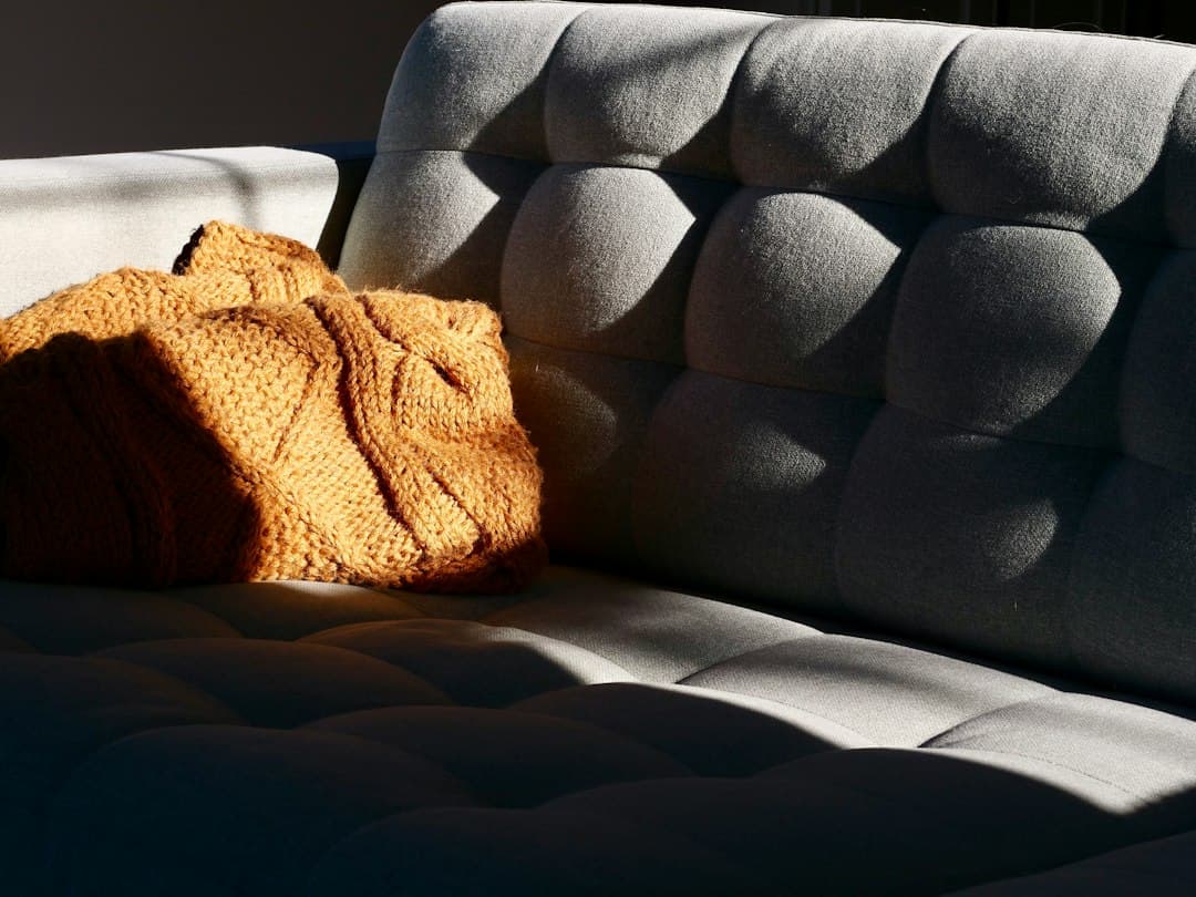 A knitted mustard yellow blanket over a grey sofa in warm afternoon sunlight
