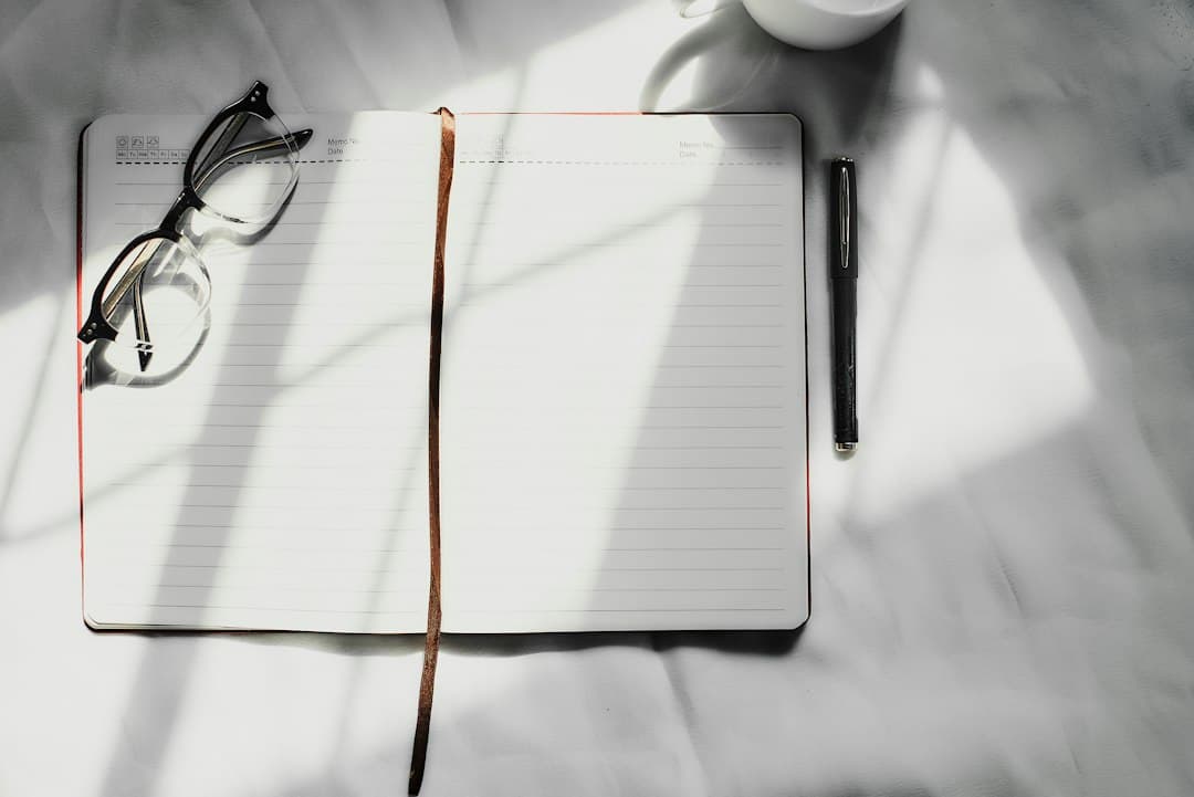 An open notebook with a pen, a pair of glasses, and a cup of coffee on a white surface