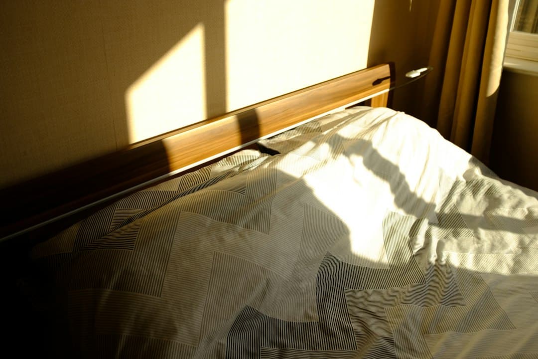 An empty bed with white sheets in soft sunlight and window shadows