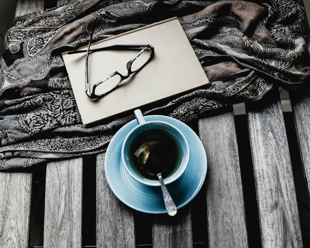 A blue ceramic teacup beside an open book on a table in soft light