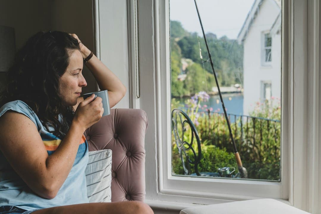 A woman with a cup of tea looking out a window at a river