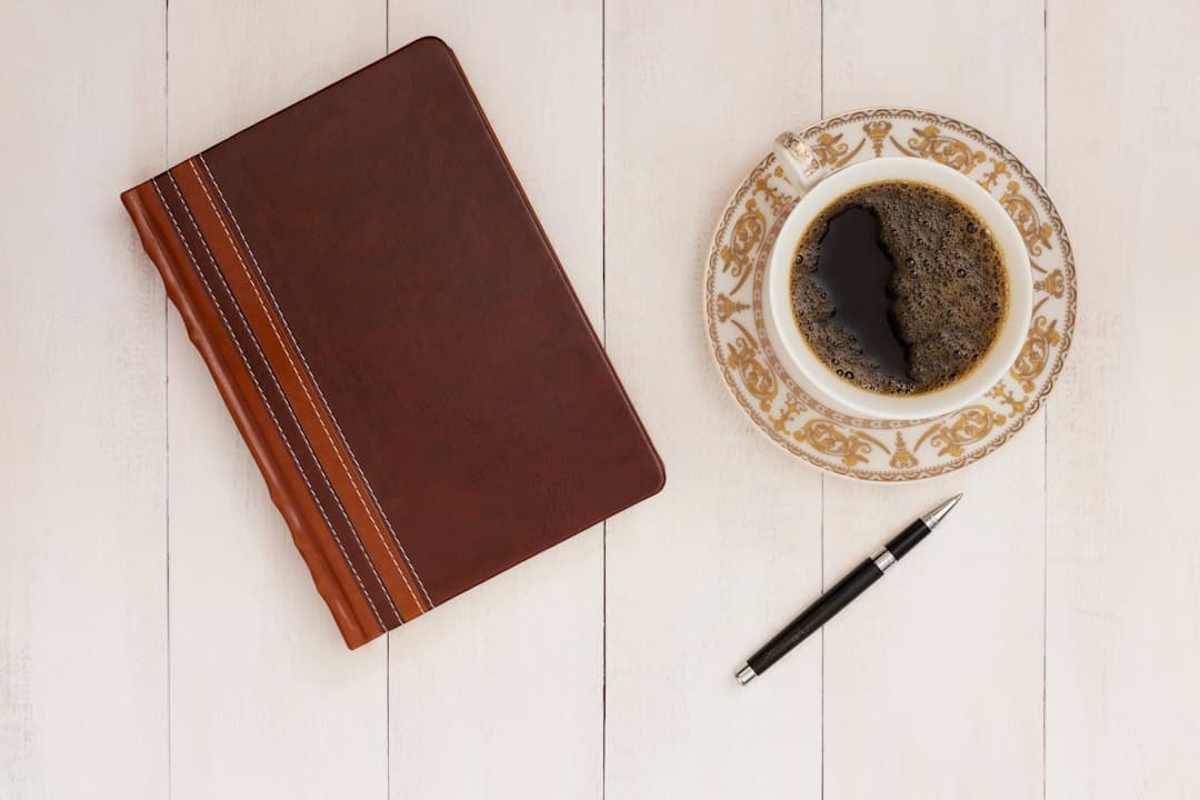 A cup of coffee beside an open notebook and a pen on a wooden table