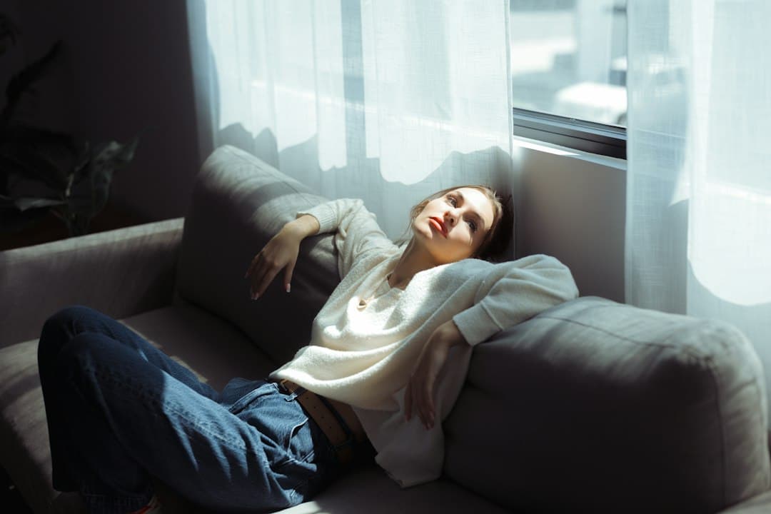 A woman in a white sweater and blue jeans resting on a grey sofa